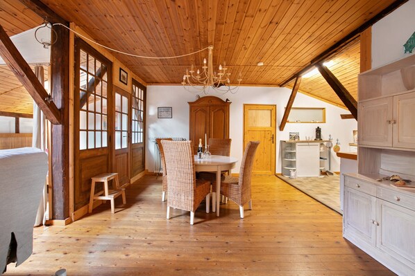 A wooden interior with a dining table, chairs, a chandelier, and a kitchen area.