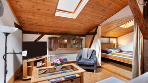 A cozy room with a wooden ceiling, a television, a sofa, a bed, and a window.