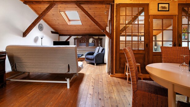 A room with a loft bed, a dining table with chairs, a chandelier, and a view of the outside through a window.