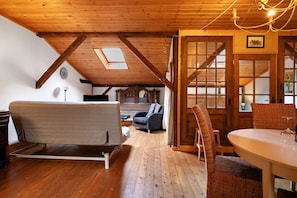 A room with a loft bed, a dining table with chairs, a chandelier, and a view of the outside through a window.