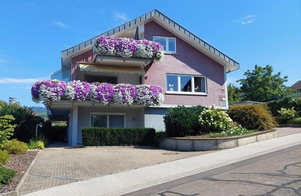 A two-story house with a balcony on the first floor and a second balcony on the second floor, both adorned with flower boxes.