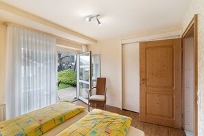 A room with two beds, a chair, a wooden door, and a view through a glass door.