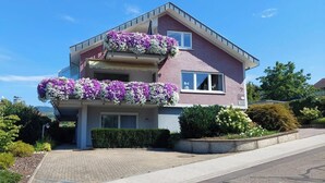 Une maison à deux étages dotée d’un balcon au premier étage et d’un deuxième balcon au deuxième étage, les deux étant ornés de jardinières.