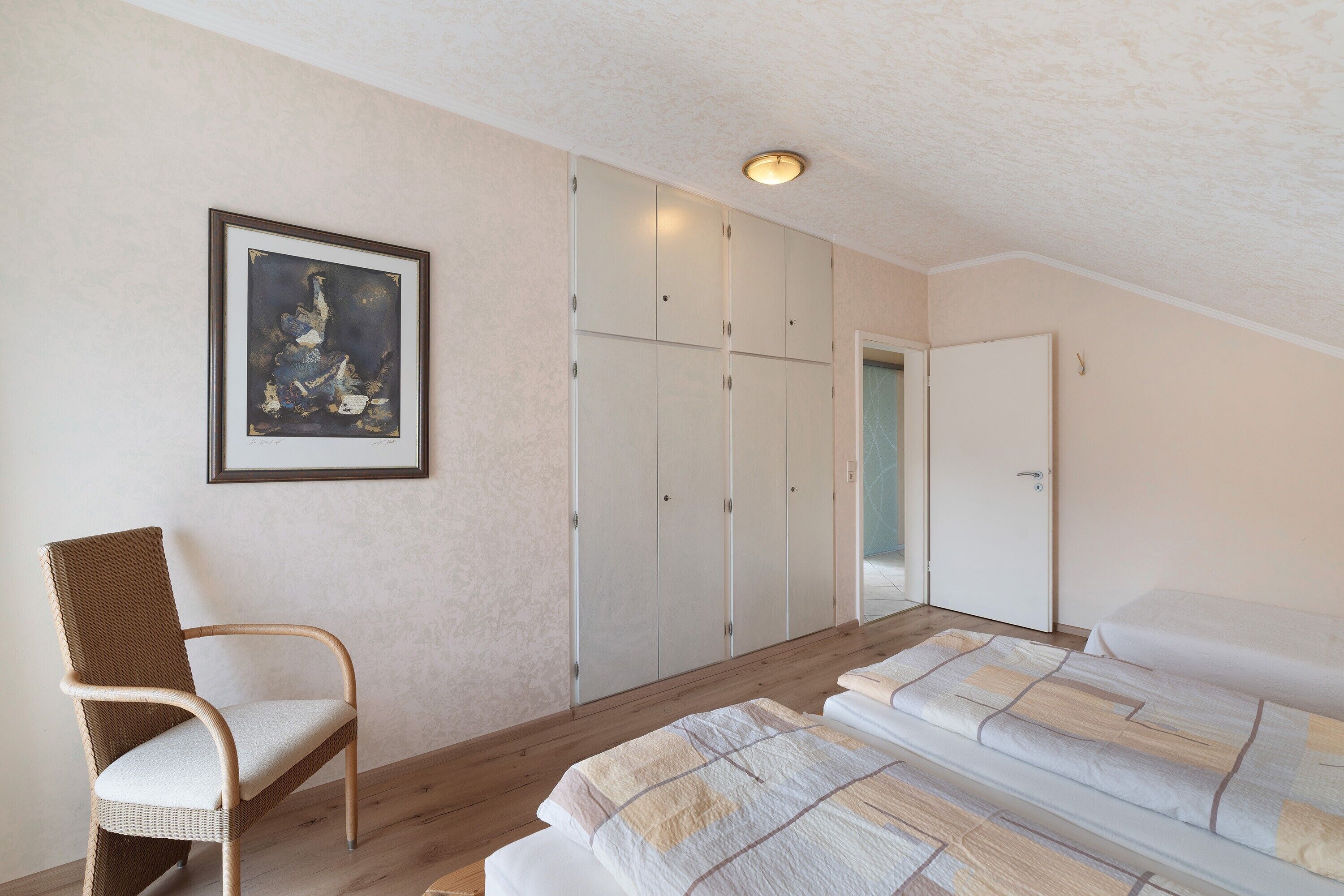 A bedroom with a bed, a chair, a wardrobe, and a framed picture on the wall.