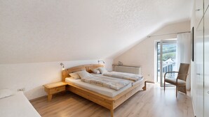 Une chambre avec un plafond en pente, un lit en bois, une table de chevet, une chaise et une vue par la fenêtre.