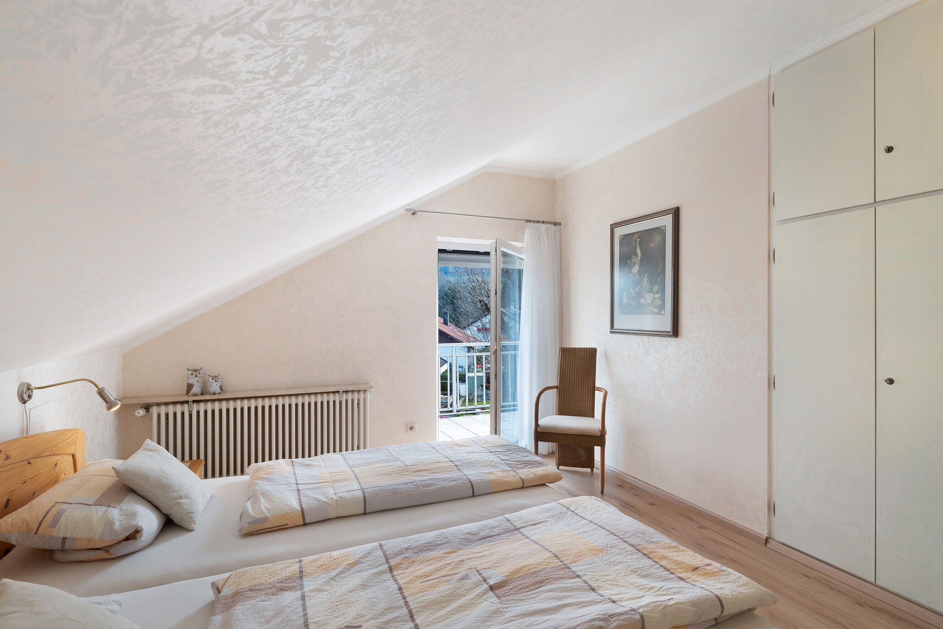 A bedroom with two beds, a radiator, a chair, and a wardrobe.