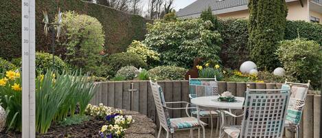 A patio with a table and chairs, surrounded by a garden with various plants and flowers.