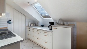 Une cuisine dotée d’une lucarne, de meubles blancs, d’un plan de travail et d’un évier.