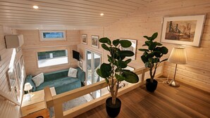 A wooden cabin interior with a sofa, a potted plant, a lamp, and a framed picture on the wall. - Tiny Home 'Tiny House Nr 3' with private terrace, Wi-Fi and air conditioning (Schwielowsee)
