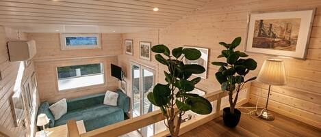 Interior de una cabaña de madera con un sofá, una planta en maceta, una lámpara y un cuadro en la pared.