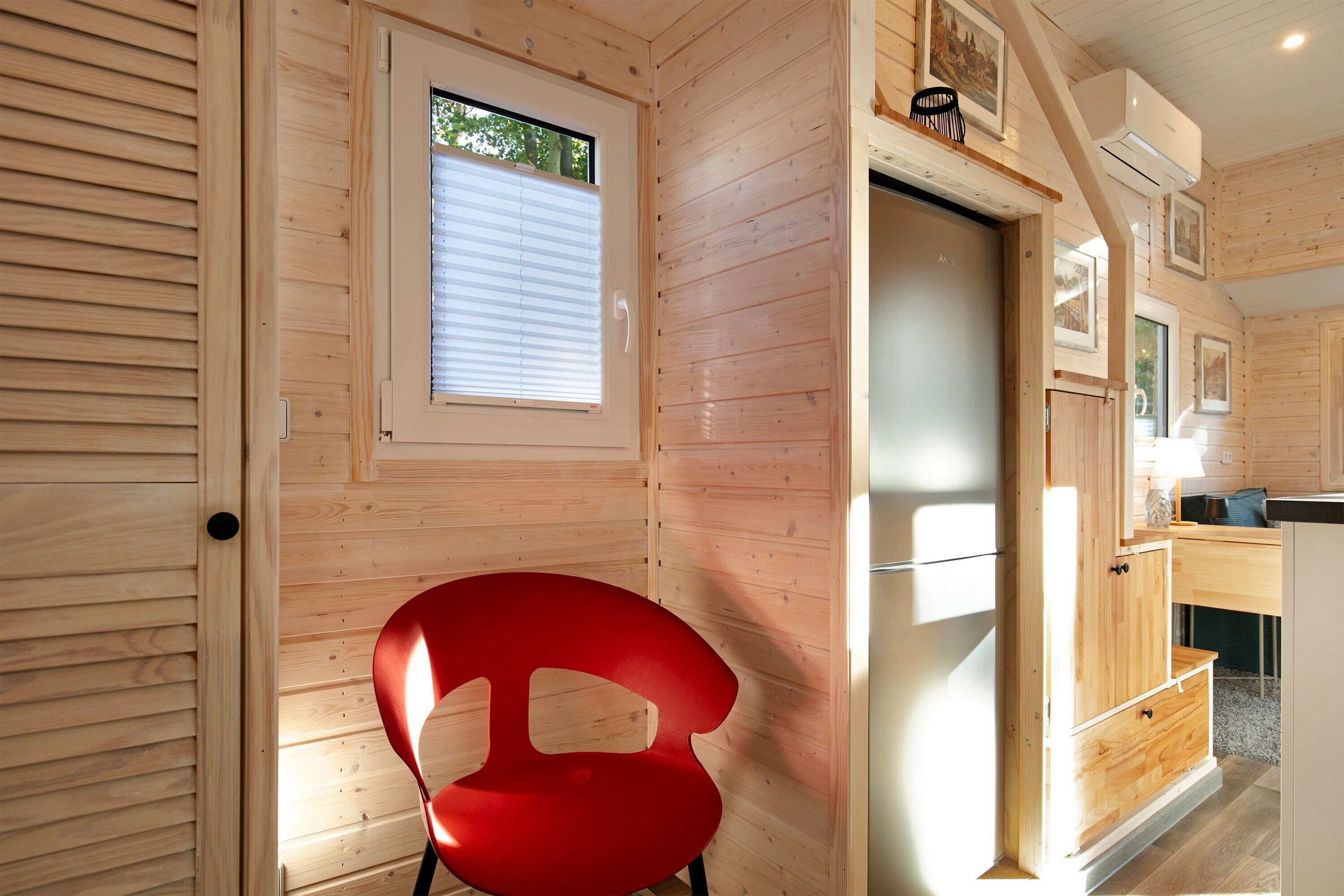 A wooden interior with a red chair, a door, and a window.