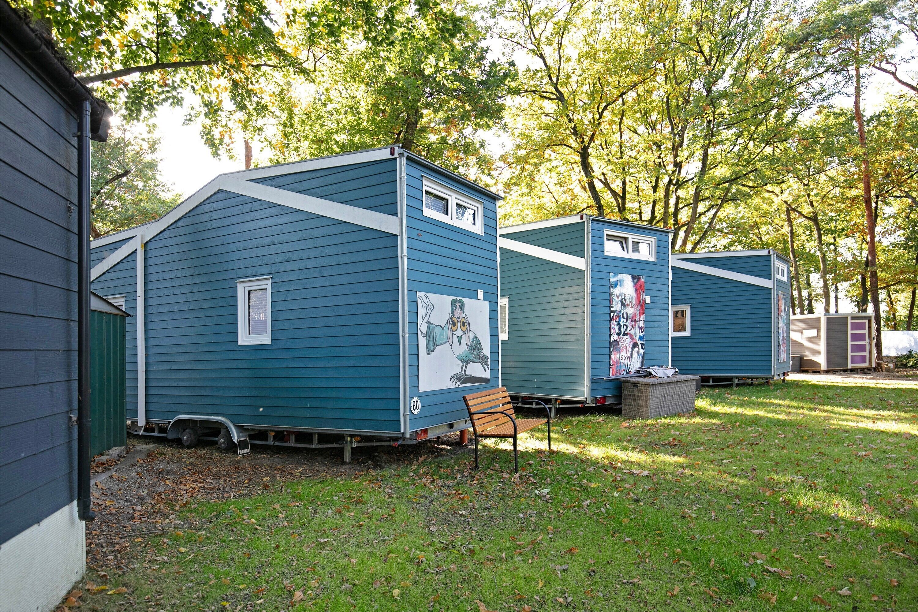Une rangée de maisons mobiles bleues, dotées de fenêtres et d’un banc devant chacune.