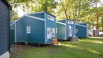 Une rangée de maisons mobiles bleues, dotées de fenêtres et d’un banc devant chacune.