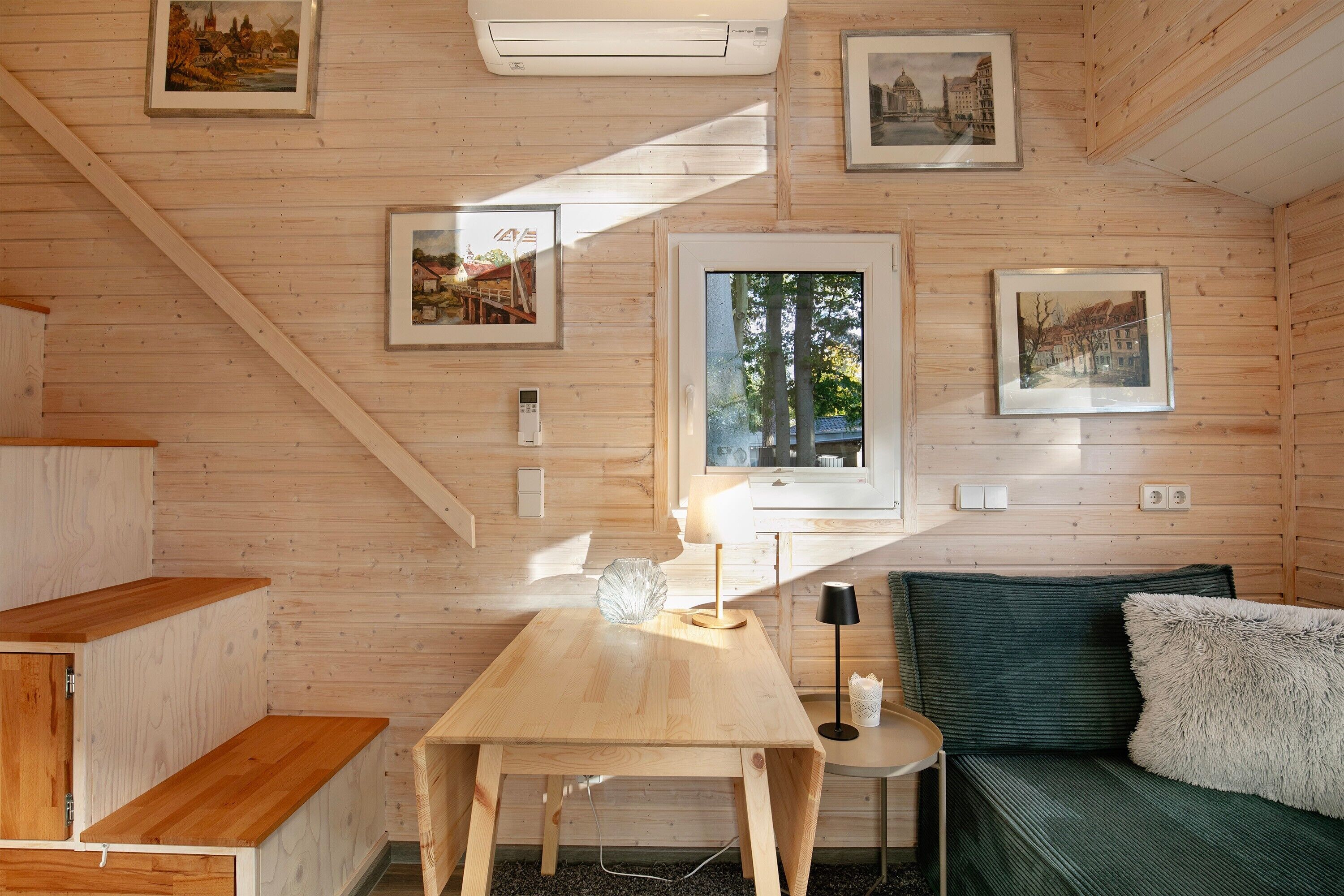 Interior de una cabaña de madera con una mesa, un sofá y cuadros en las paredes.