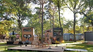 A wooden deck with outdoor furniture, a small stage, and a building with a mural. - Tiny Home 'Tiny House Nr 3' with private terrace, Wi-Fi and air conditioning (Schwielowsee)