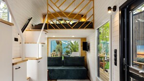 A compact room with a loft bed, built-in storage, a sofa, and a large sliding glass door leading to an outdoor area.