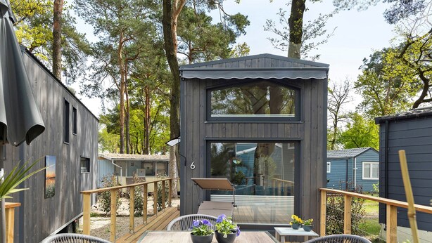 A wooden deck with a table and chairs, surrounded by cabins.