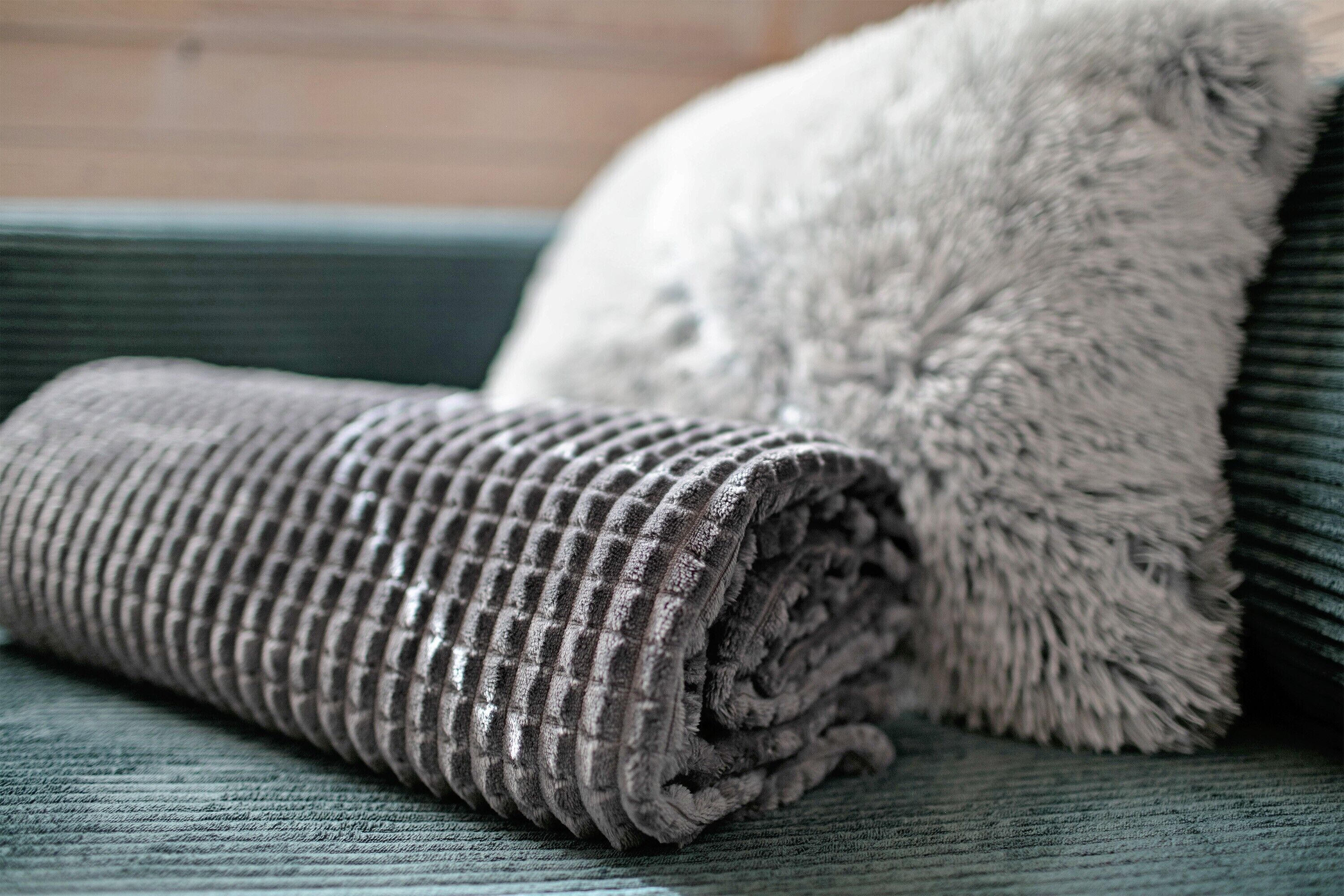 A rolled-up textured blanket and a fluffy pillow on a green upholstered sofa.