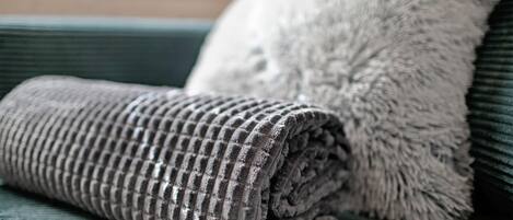 A rolled-up textured blanket and a fluffy pillow on a green upholstered sofa.