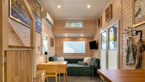 L’intérieur chaleureux d’un chalet avec un coin repas en bois, un canapé vert, une petite table et un téléviseur fixé au mur.