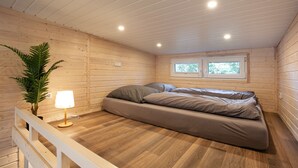 Une pièce de cabane en bois comprenant un lit, une plante en pot et une fenêtre.