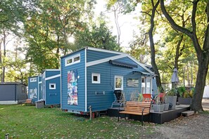 Une maison mobile bleue avec un petit porche, un banc et des plantes en pot.