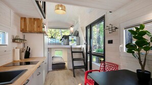 A compact kitchen with a wooden countertop, a built-in stove, and a small dining area with a table and chairs. - Tiny Home 'Tiny House Nr 4' with private terrace, Wi-Fi and air conditioning (Schwielowsee)