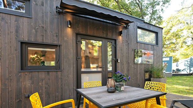 A wooden structure with a table and yellow chairs, a window, and a door. - Tiny Home 'Tiny House Nr 4' with private terrace, Wi-Fi and air conditioning (Schwielowsee)