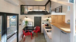 A modern kitchen with a dining area, a loft bedroom, and a view of the outdoors. - Tiny Home 'Tiny House Nr 4' with private terrace, Wi-Fi and air conditioning (Schwielowsee)