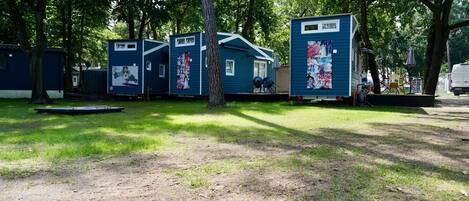 A row of blue mobile homes with a grassy yard, trees, and a small table.