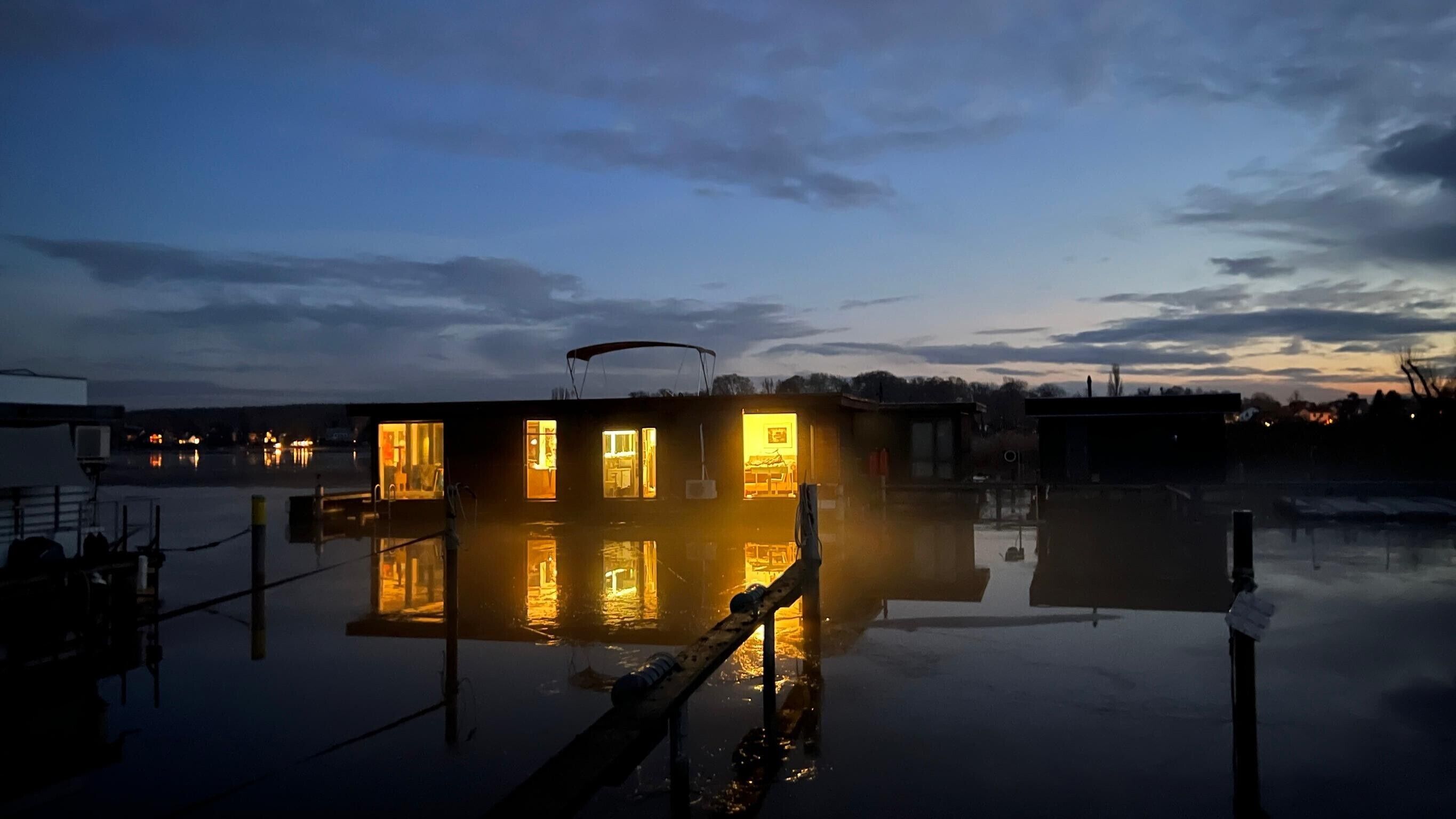 A floating structure with multiple illuminated windows, surrounded by calm water.