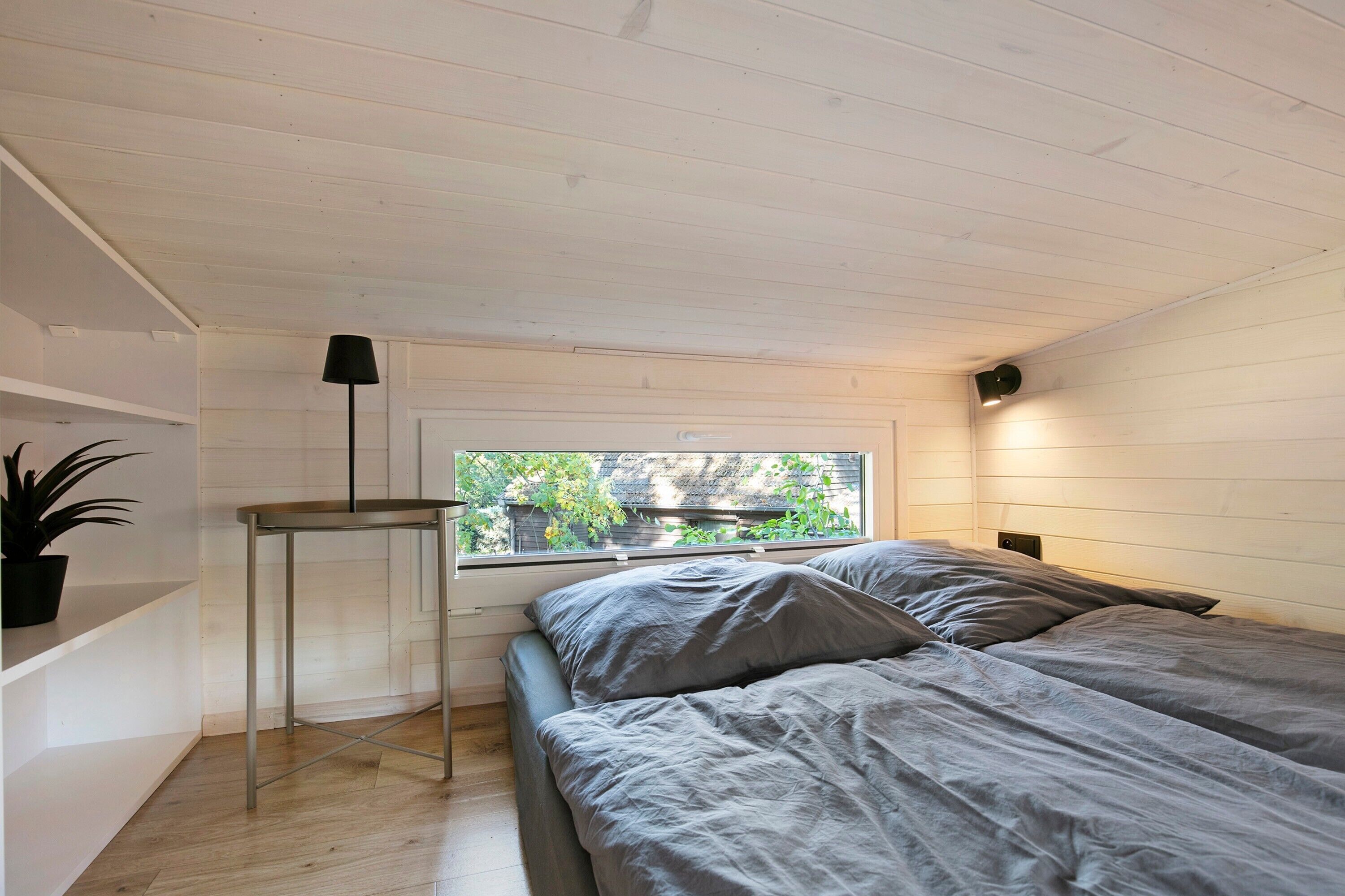 A bedroom with a bed, a window, a plant, and a table.