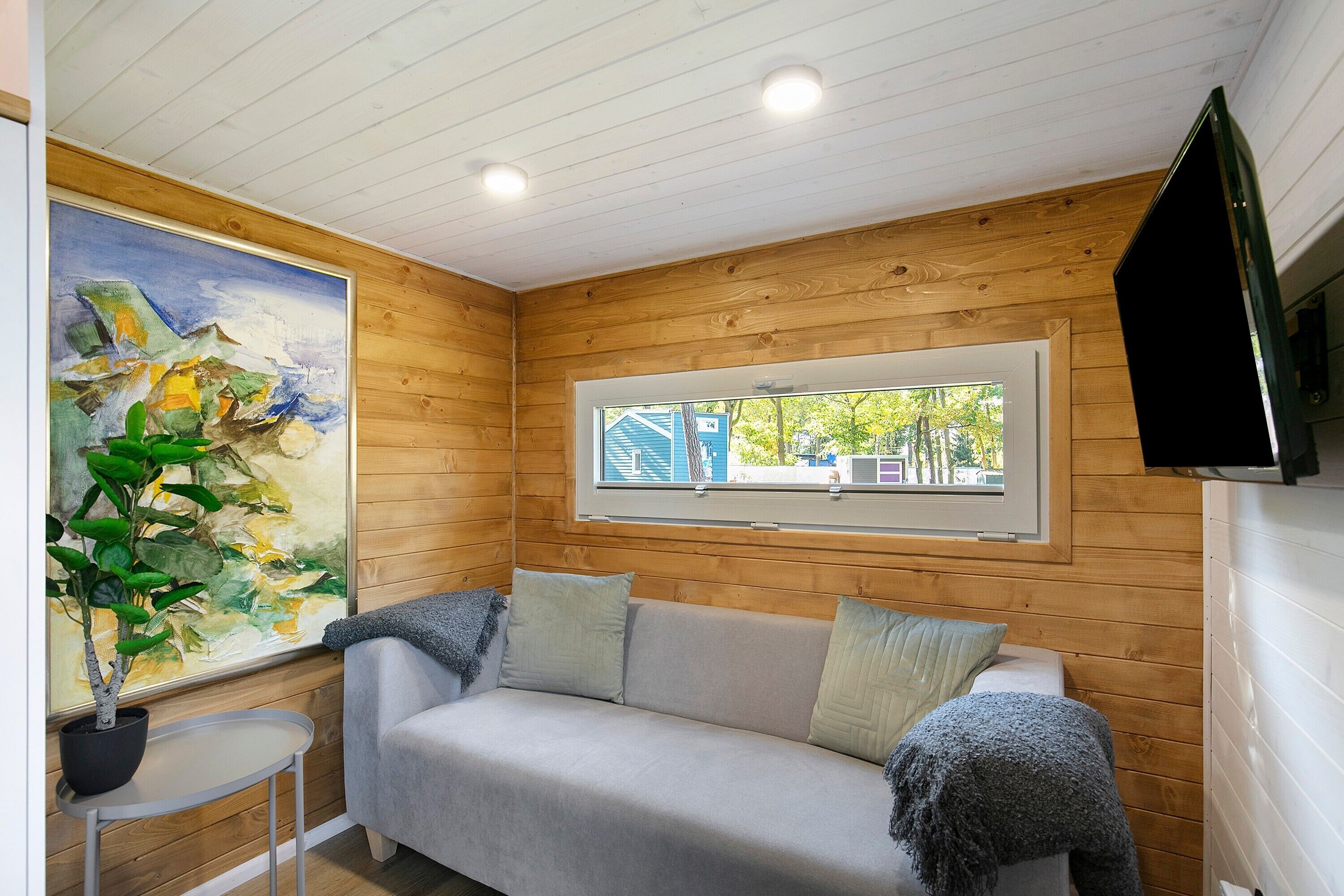 A wooden-paneled room with a sofa, a painting, a window, and a television.