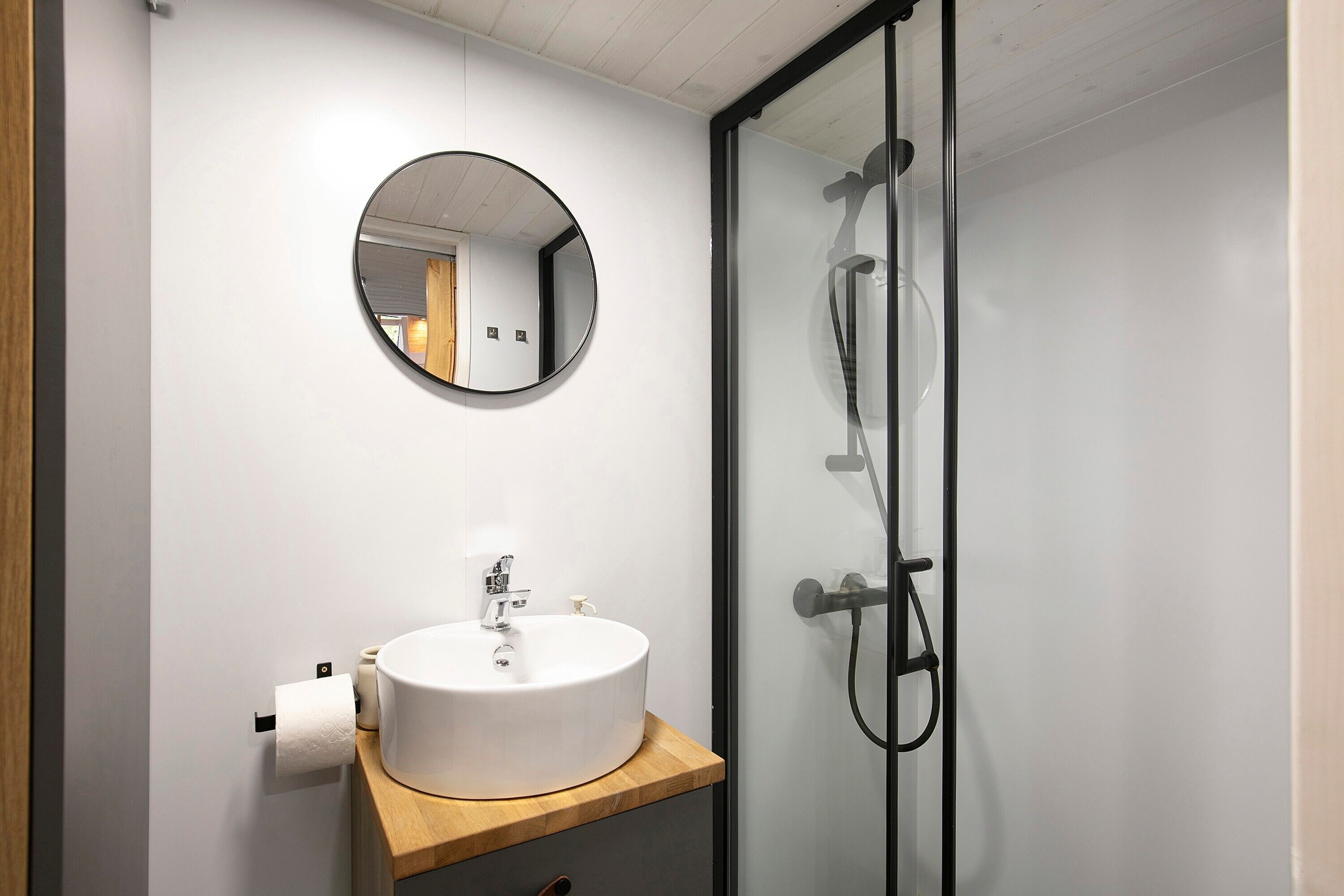 A bathroom with a white sink, a round mirror, and a glass shower enclosure.