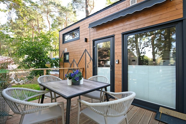 A wooden deck with a table and wicker chairs, surrounded by trees.