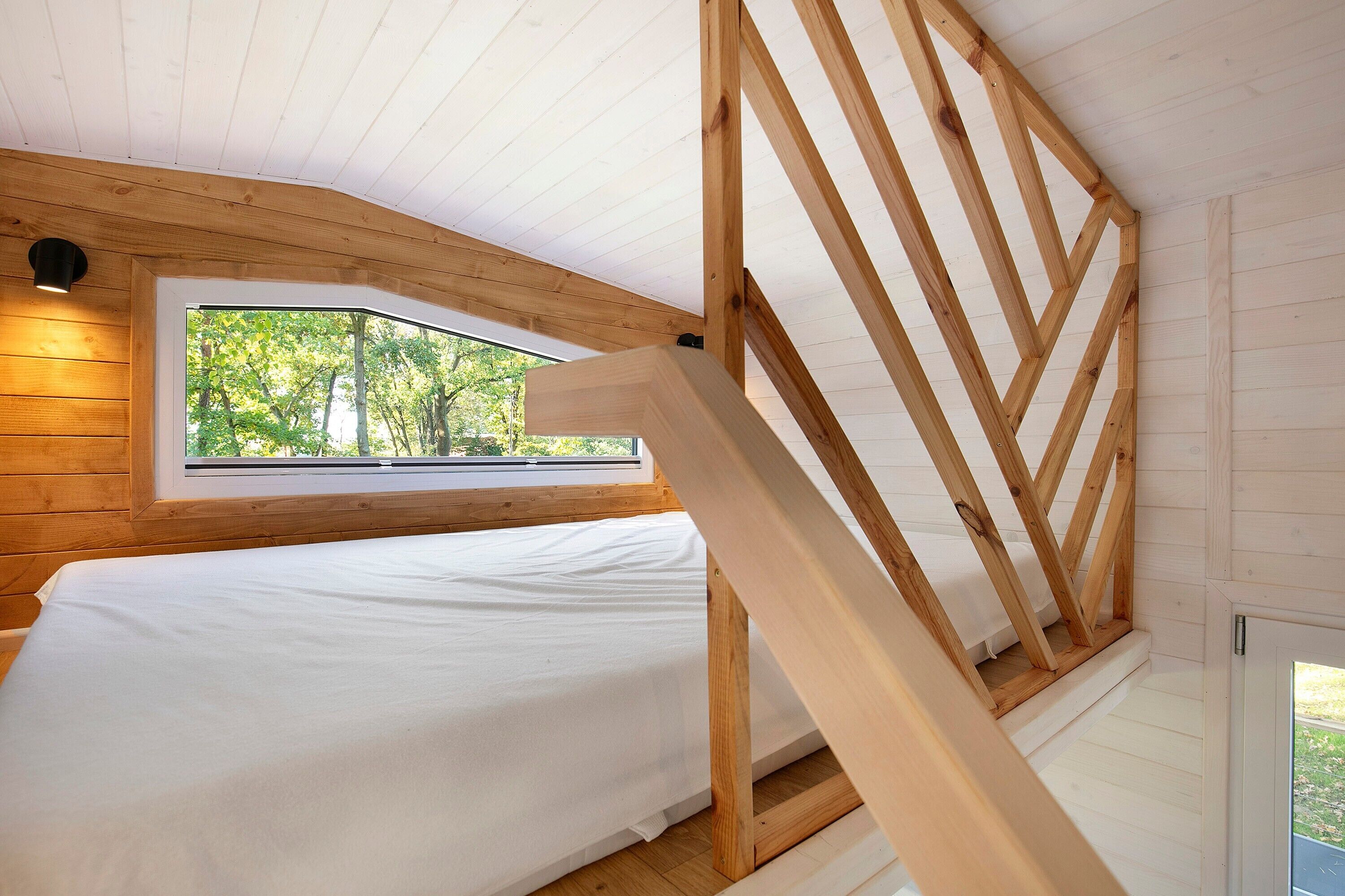 A bedroom with a wooden ceiling, a bed, a window, and a staircase.