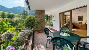 Un patio con tavolo e sedie, un pilastro in pietra, piante in vaso e vista su un paesaggio montuoso.