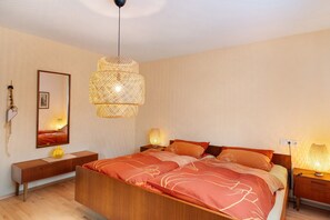 A bedroom with a bed, bedside tables, a hanging light fixture, and a mirror.