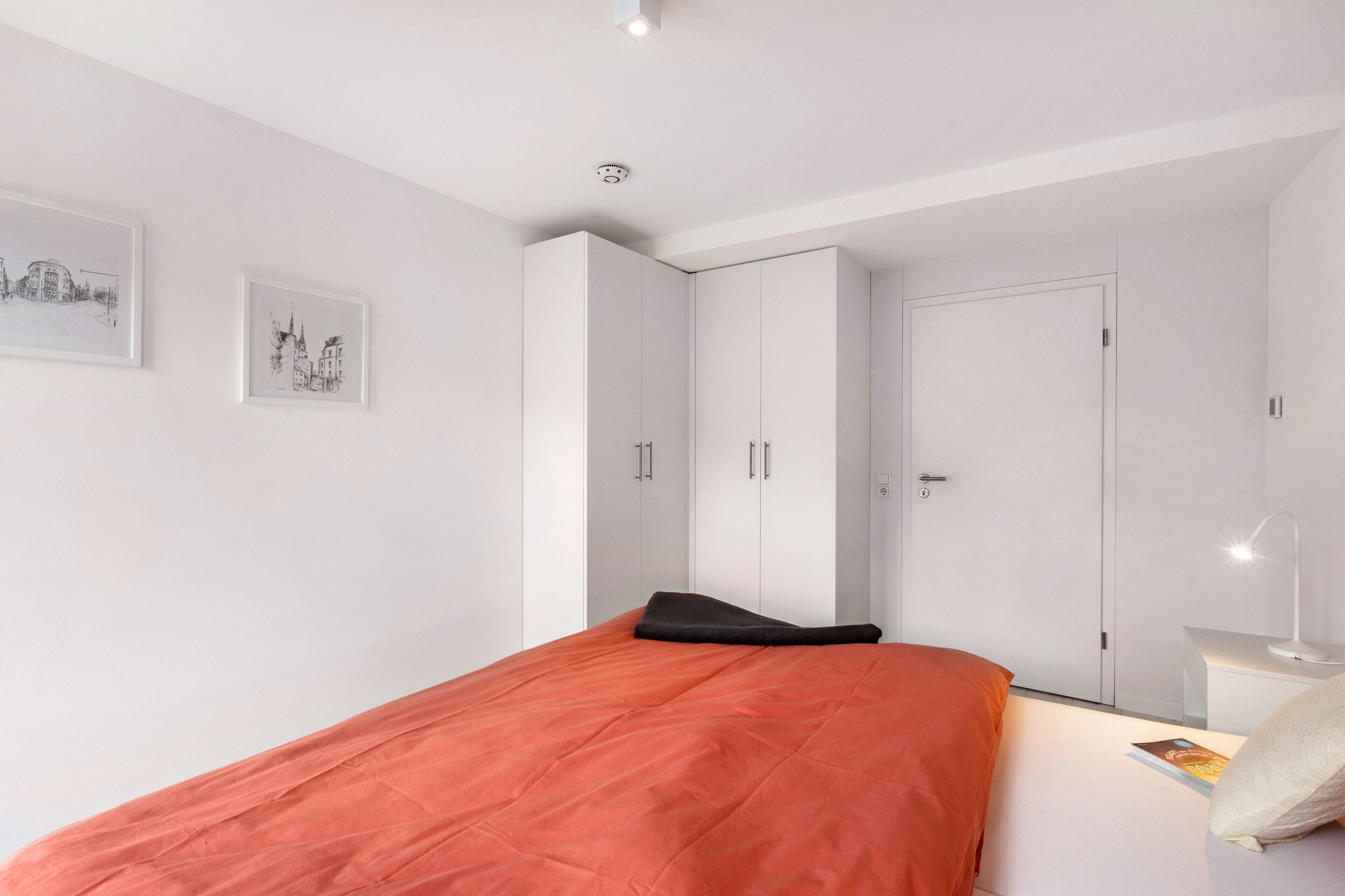 Un dormitorio con cama, armario blanco y mesita de noche con lámpara.