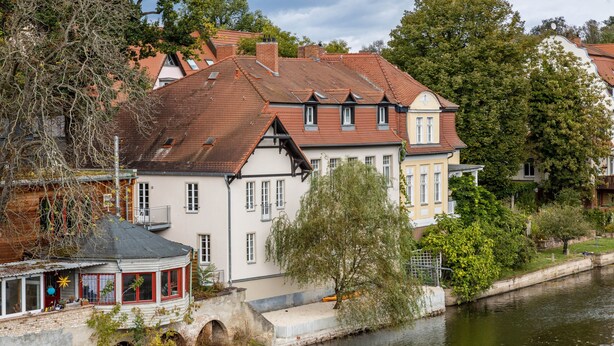 Un edificio a la orilla del río con un estilo arquitectónico tradicional, con múltiples ventanas y un balcón destacado.