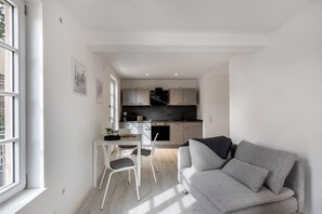 Un soggiorno moderno con un divano grigio, un tavolo da pranzo con sedie e una cucina sullo sfondo.