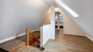 Een modern interieur met een houten trap, witte muren en een schuin dak met dakraam.