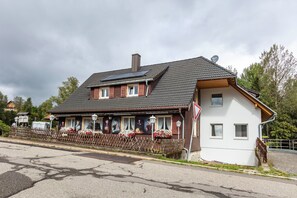 Un bâtiment à deux étages, doté d’un toit en pente, d’une petite dépendance attenante et d’une clôture en bois.