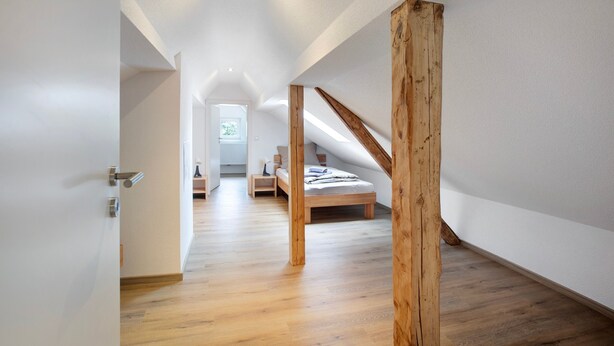 Een moderne loft slaapkamer met een schuine plafond, houten balken, een houten bed en een gang naar een badkamer.