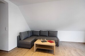 Une pièce d’angle avec un canapé d’angle gris, une table basse en bois et un sol carrelé.