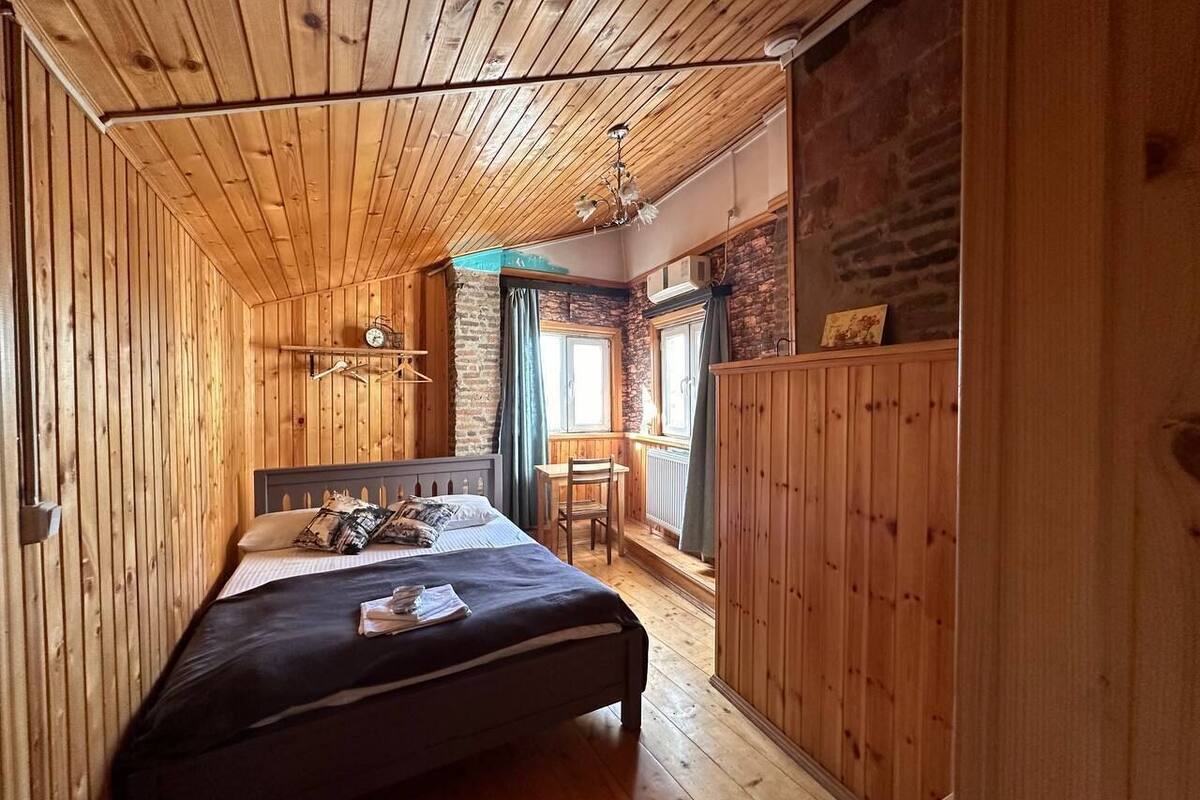 A wooden-paneled bedroom with a bed, a chair, and a small table.