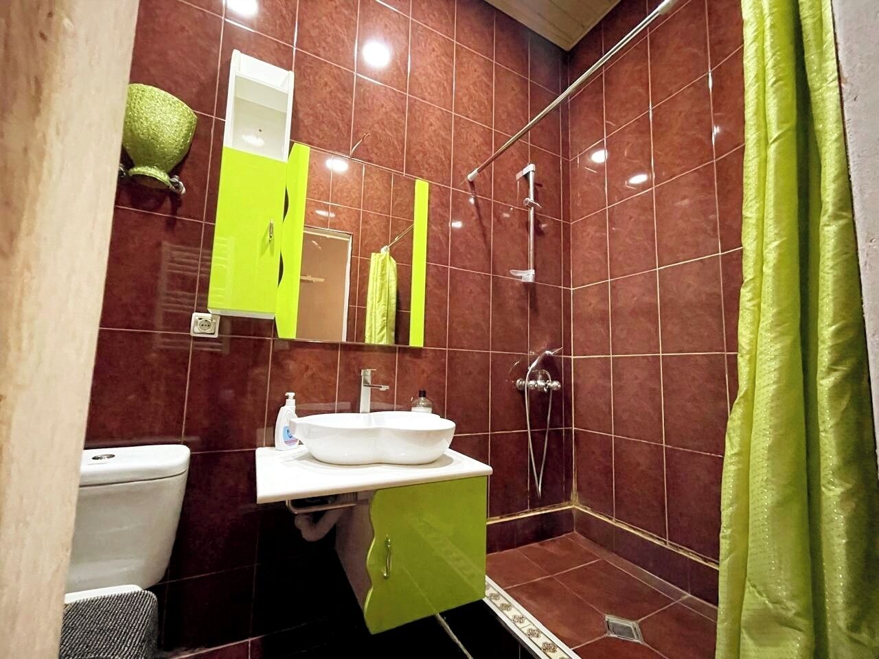 A bathroom with a white sink, green cabinet, and a shower with a green curtain.