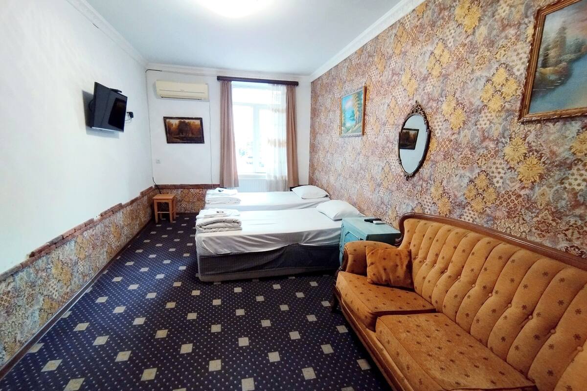 A hotel room with a patterned floor, a sofa, a bed with two pillows, a small table, and a television mounted on the wall.
