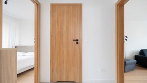 A modern hotel room with a wooden door, a bed, a desk, and a chair.