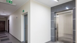 Un ascenseur moderne avec une finition métallique, un couloir doté d’un sol à motifs et un panneau indiquant la sortie de secours.